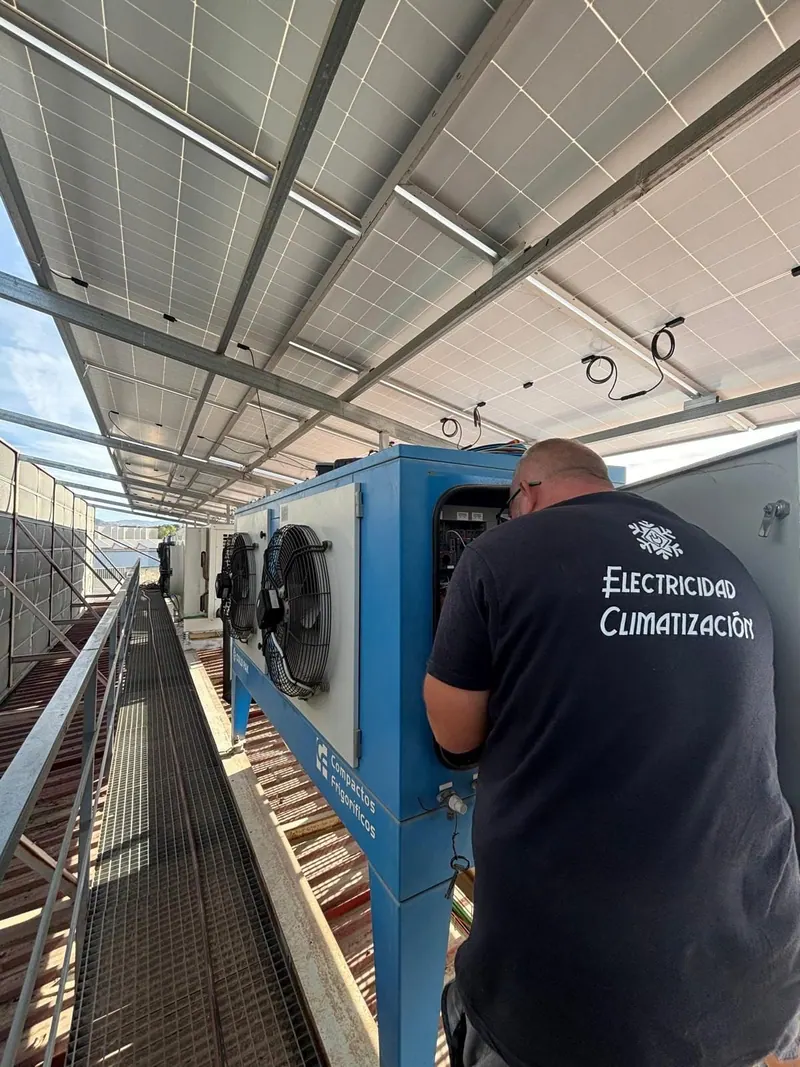 ITAFE technician checking a refrigeration unit on a rooftop, beneath a solar installation